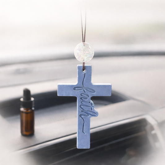 Cross-shaped car air freshener with 'faith' text on a car rear view mirror.