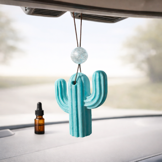Teal cactus-shaped car air freshener hanging from a car's rearview mirro.